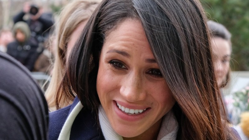 Meghan Markle greets the crowd while wearing a navy colored coat