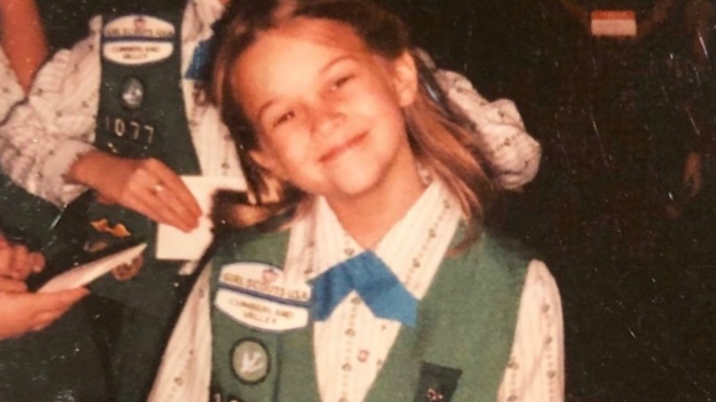 A young Reese Witherspoon tilts her head to the side while wearing an old fashioned Girl Scout uniform