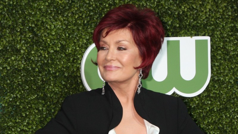 Sharon Osbourne, in a black blazer, looks off to the side