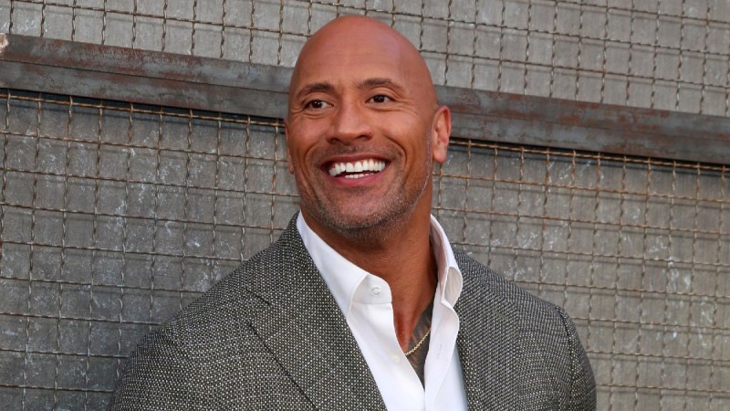 Dwayne The Rock Johnson wears a gray suit against a gray wall
