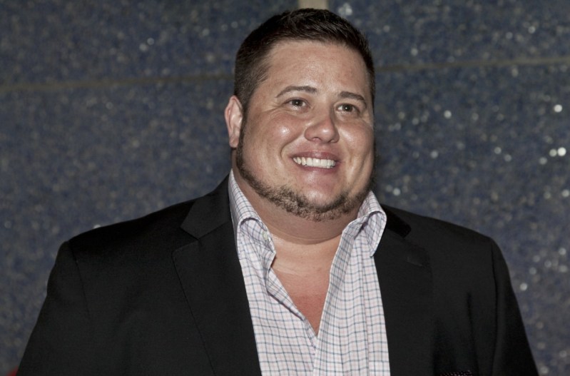 Chaz Bono smiling and wearing a black blazer with a white shirt.