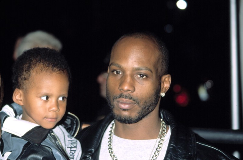 DMX wearing a black leather jacket and a silver chain while holding one of his children.