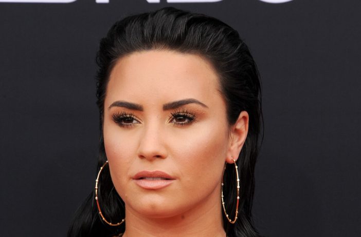 Demi Lovato sporting a slicked back hairstyle and hoop earrings
