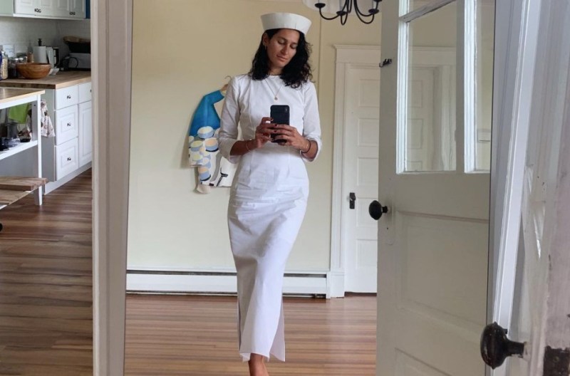 Elena Moussa taking a selfie while wearing a white dress and a white hat.