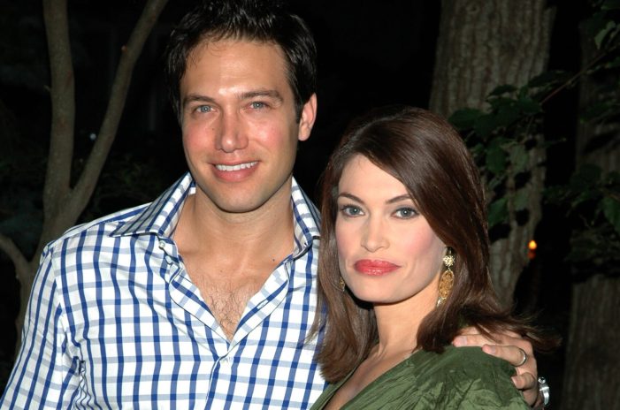 Eric Villency is wearing a blue and white checkered shirt. His arm is around his wife, Kimberly Guilfoyle, who is wearing red lipstick and a green dress.