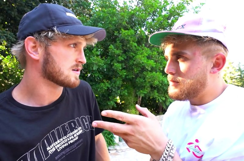 Logan Paul in a black hat and black shirt standing face-to-face with Jake Paul, who is wearing a white shirt and a pink hat.