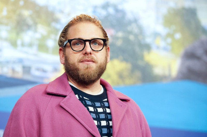 Jonah Hill wearing a pink blazer, black glasses, and a blue patterned shirt.