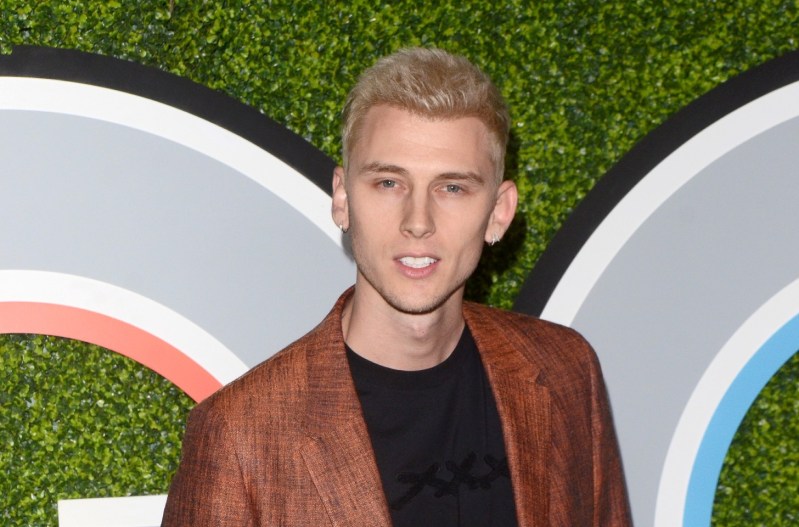 MGK smiling and wearing a red suit with a black shirt.