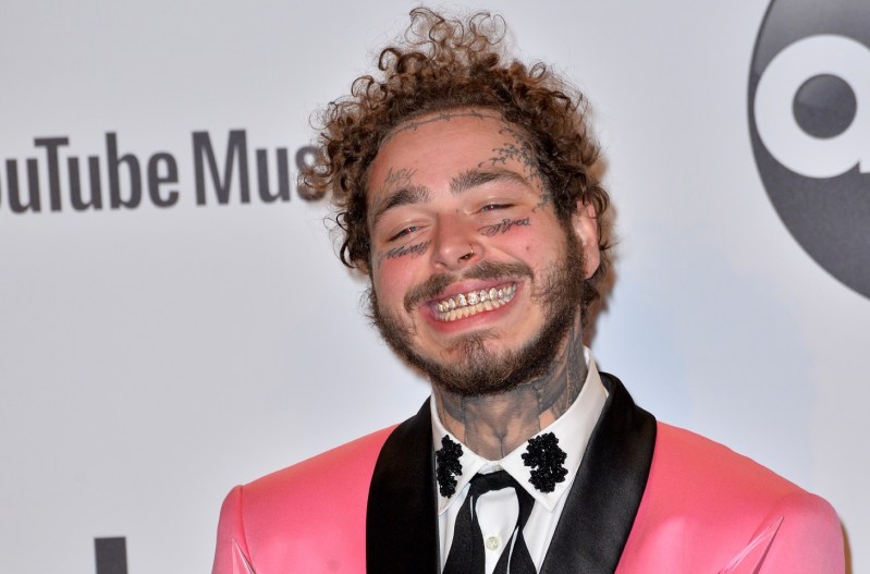 Post Malone grinning and wearing a pink suit.