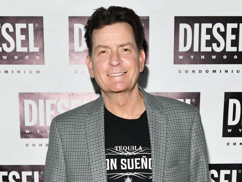 Charlie Sheen smiling in plaid suit jacket with black shirt underneath