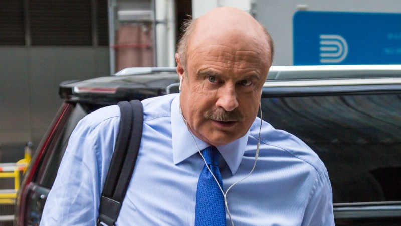 Dr. Phil McGraw wears a blue shirt and tie as he exits a car