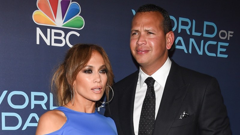 Jennifer Lopez, in a blue dress, poses with Alex Rodriguez, in a dark suit, on the red carpet