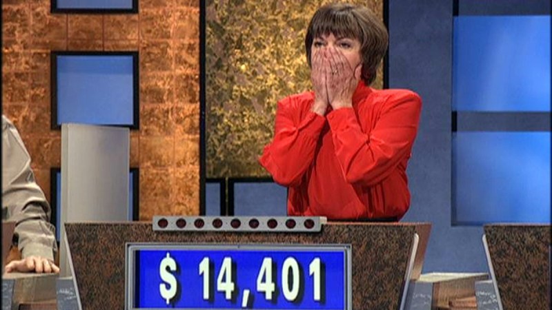 A contestant on Jeopardy! covers her face in surprise with both hands