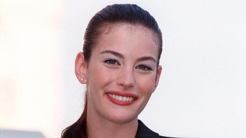 Liv Tyler smiles at the camera while wearing a black suit outdoors