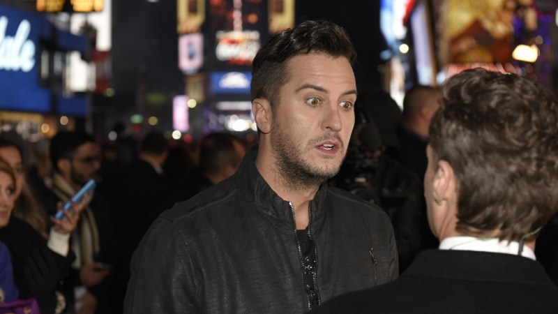 Luke Bryan, wearing a black jacket speaks to a man in Times Square