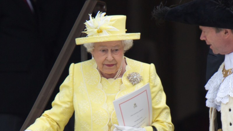 Queen Elizabeth wears a yellow hat and dress as she walks down a flight of stairs