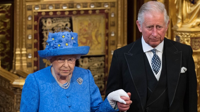 Queen Elizabeth, wearing all blue, walks through Parliament with Prince Charles, in a dark suit