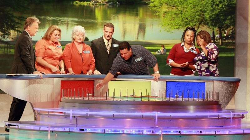 A contestant spins the wheel as others look on in an episode of Wheel Of Fortune