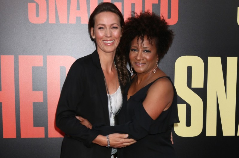 Wanda Sykes and her wife, Alex Sykes, both wearing black and hugging each other on the red carpet.