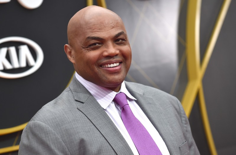Charles Barkley smiling and wearing a grey suit with a purple tie.