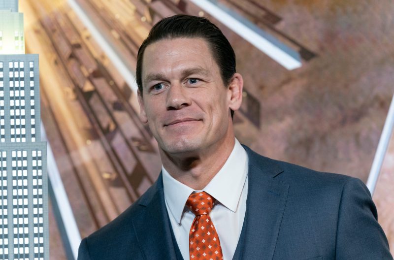 John Cena with slicked back hair, wearing a suit jacket and orange tie