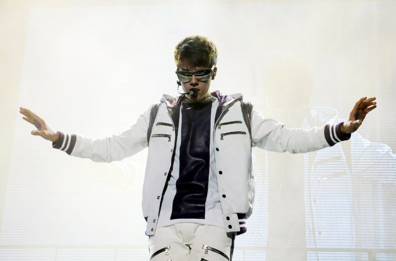 Justin Bieber in a white jacket holding his hands out to the side.
