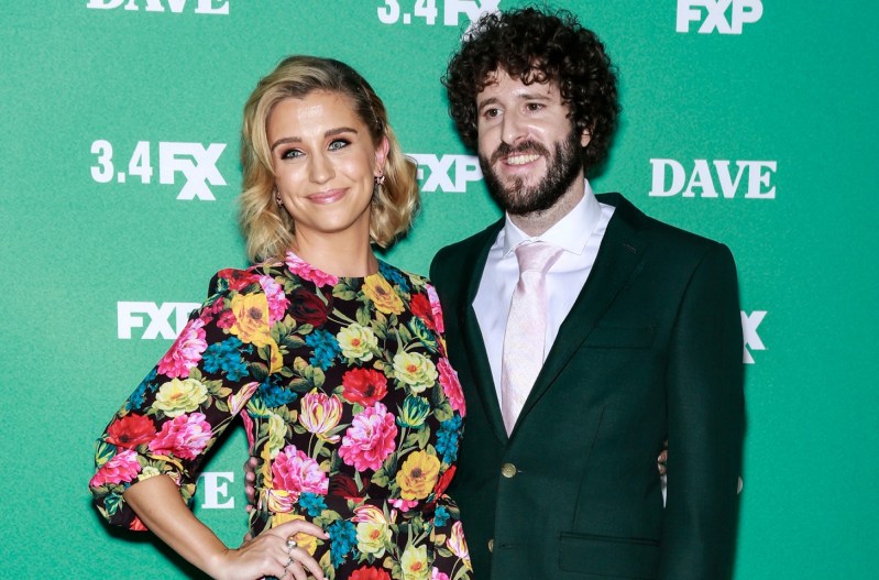 Lil Dicky in a green suit standing with Taylor Misiak who is wearing a floral dress.