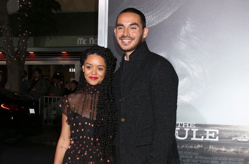 Manny Montana in a black suit with his wife, Adelfa Marr, who is wearing a black and red dress.