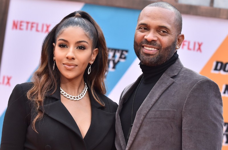 Mike Epps in a gray jacket with his wife, Kyra Robinson who is wearing a black jacket.