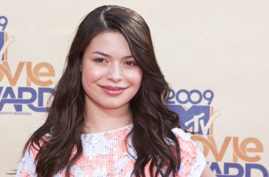Miranda Cosgrove wearing a pink and blue blouse at a red carpet event.
