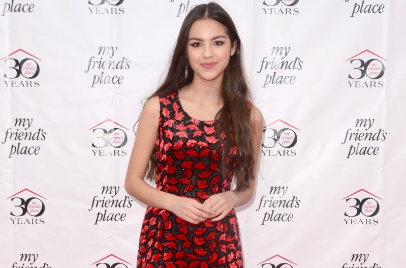 Olivia Rodrigo smiling and wearing a red and black floral dress.