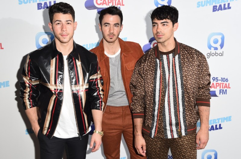 The Jonas Brothers at a red carpet event wearing multicolored bomber jackets.