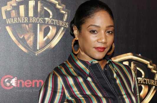 Tiffany Haddish is wearing a multicolored striped shirt with large hoop earrings.