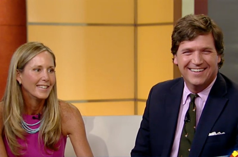 Tucker Carlson and his wife, Susan Andrews on the set of Fox News. He's wearing a navy blue suit, and she's wearing a pink dress.