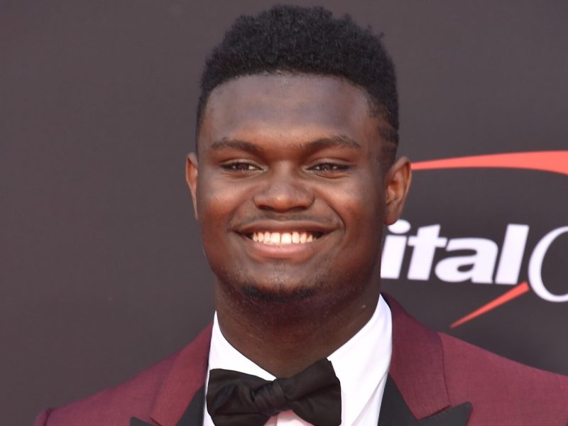 Zion Williamson smiling and wearing a red suit with a black bow tie.