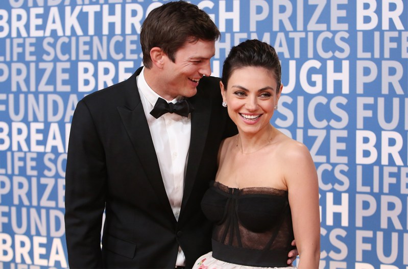 Ashton Kutcher laughing with Mila Kunis at a red carpet event