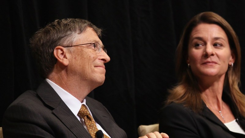 Bill Gates smiles as Melinda Gates looks over at him while the two share a stage