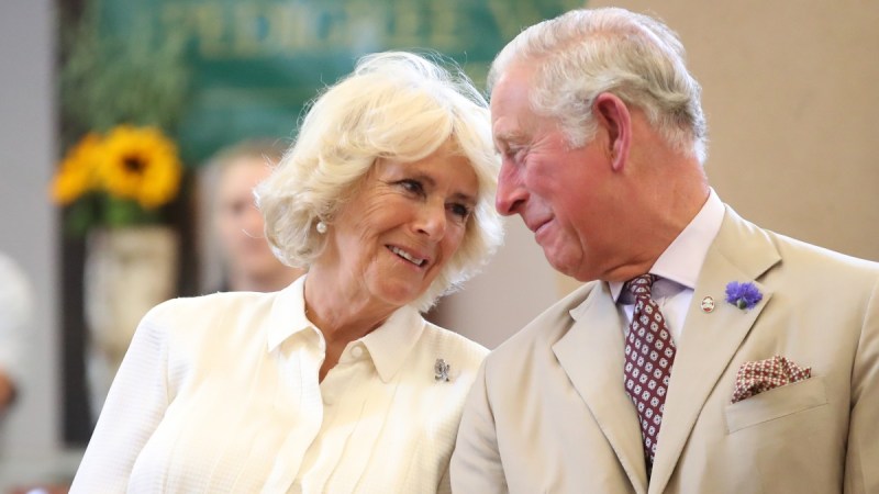 Camilla Parker Bowles, in a white blouse, leans towards Prince Charles, in a khaki suit, who smiles at her