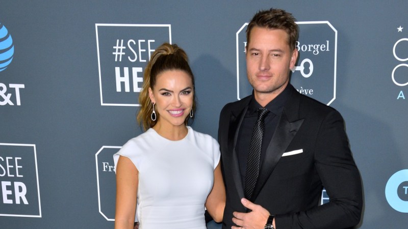 Chrishell Stause wears a white dress as she stands next to her now ex husband Justin Hartley, in a black suit