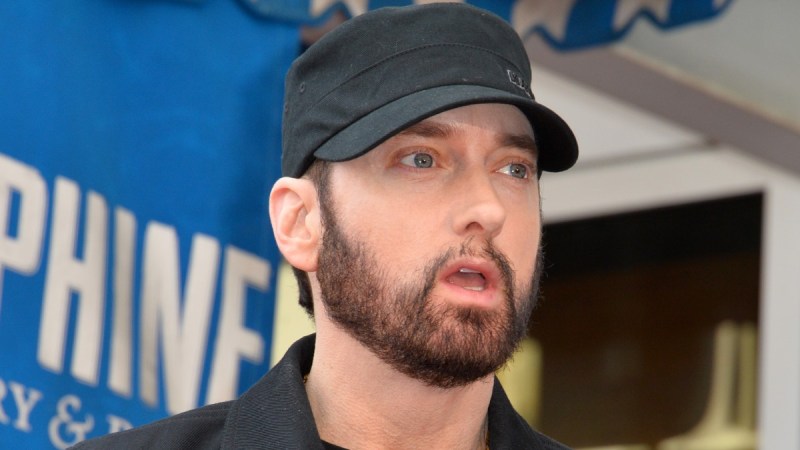 Eminem wears a dark jacket and hat as he gives a speech
