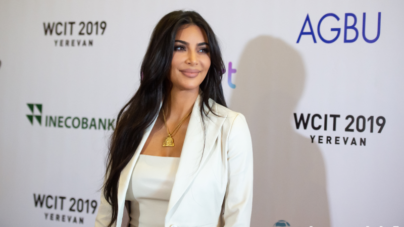Kim Kardashian wears a white suit jacket over a white top against a white background