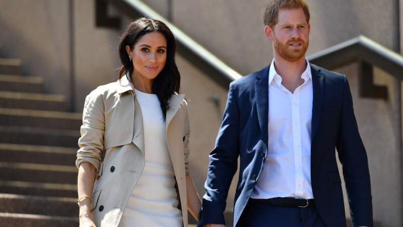 Meghan Markle, in a white dress, and Prince Harry, in a navy suit, descend a flight of stairs