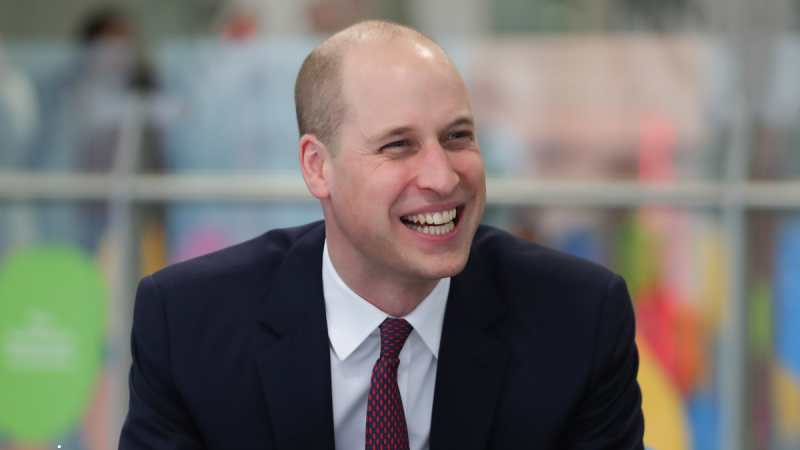 Prince William laughs in response during a public event while wearing a dark suit