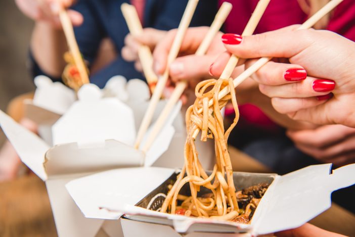 Image of Chinese food takeout while people pick the food up with chopsticks.