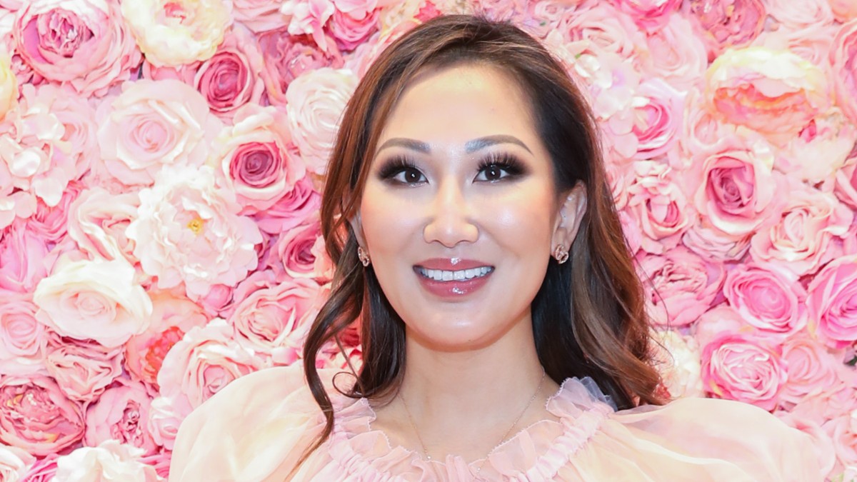 Tiffany Moon wears a gauzy pink top against a background of pink flowers