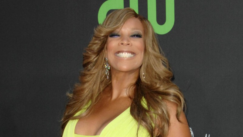 Wendy Williams wears a bright neon yellow dress against a dark backdrop
