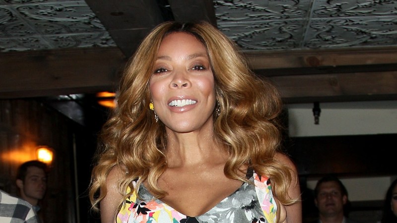 Wendy Williams wears a floral dress and smiles as she walks through an event