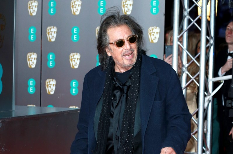 Al Pacino standing with his mouth open and wearing a blue jacket, black sunglasses, and a black scarf.