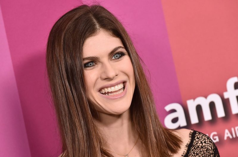 Alexanda Daddario smiling in front of a pink backgroun