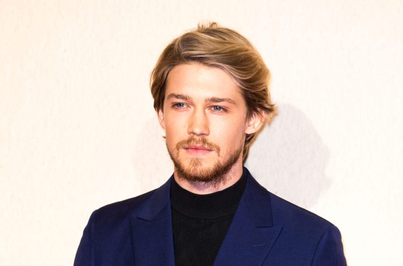 Joe Alwyn with facial hair wearing blue suit jacket